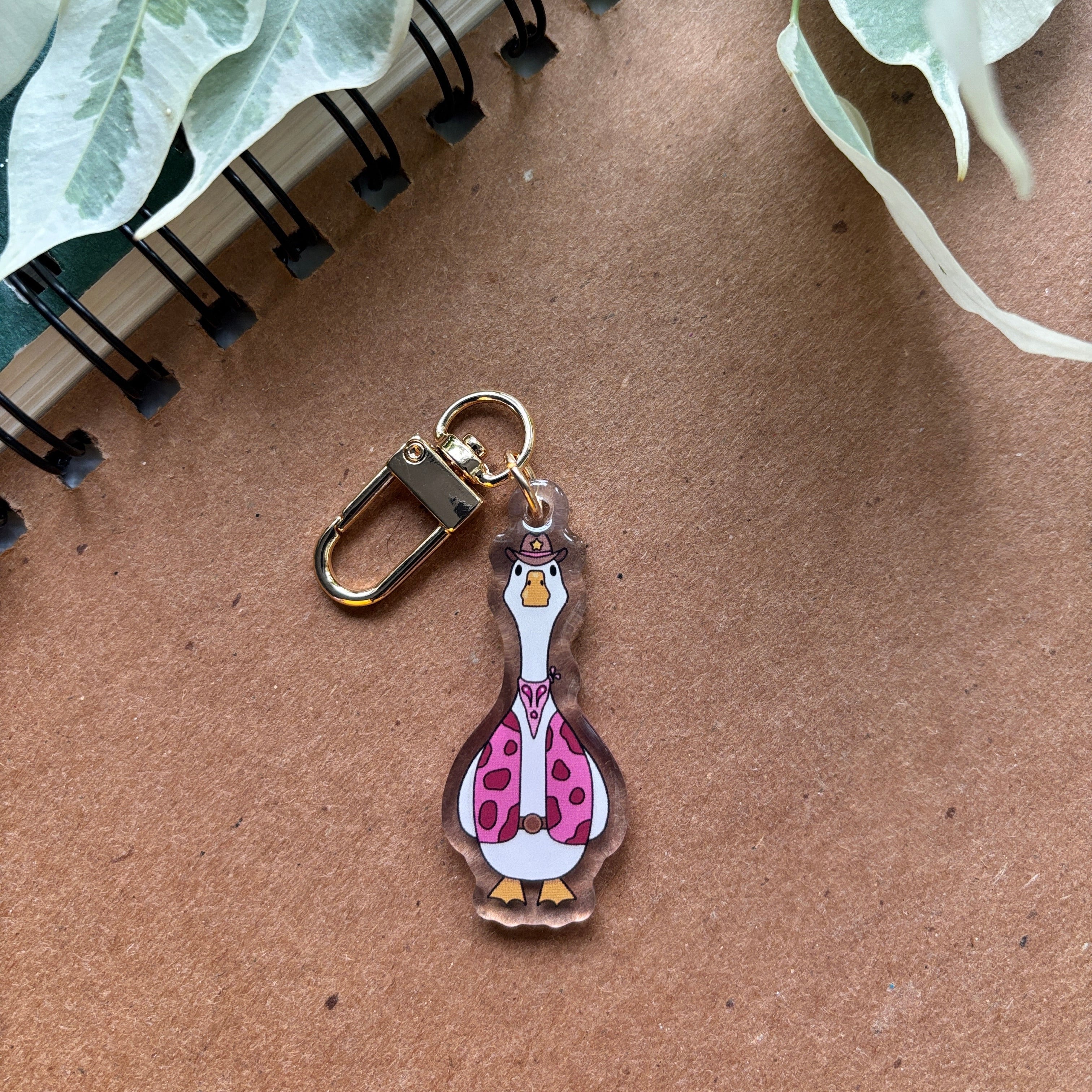 Keychain with a cartoon duck design on a brown surface with green leaves.