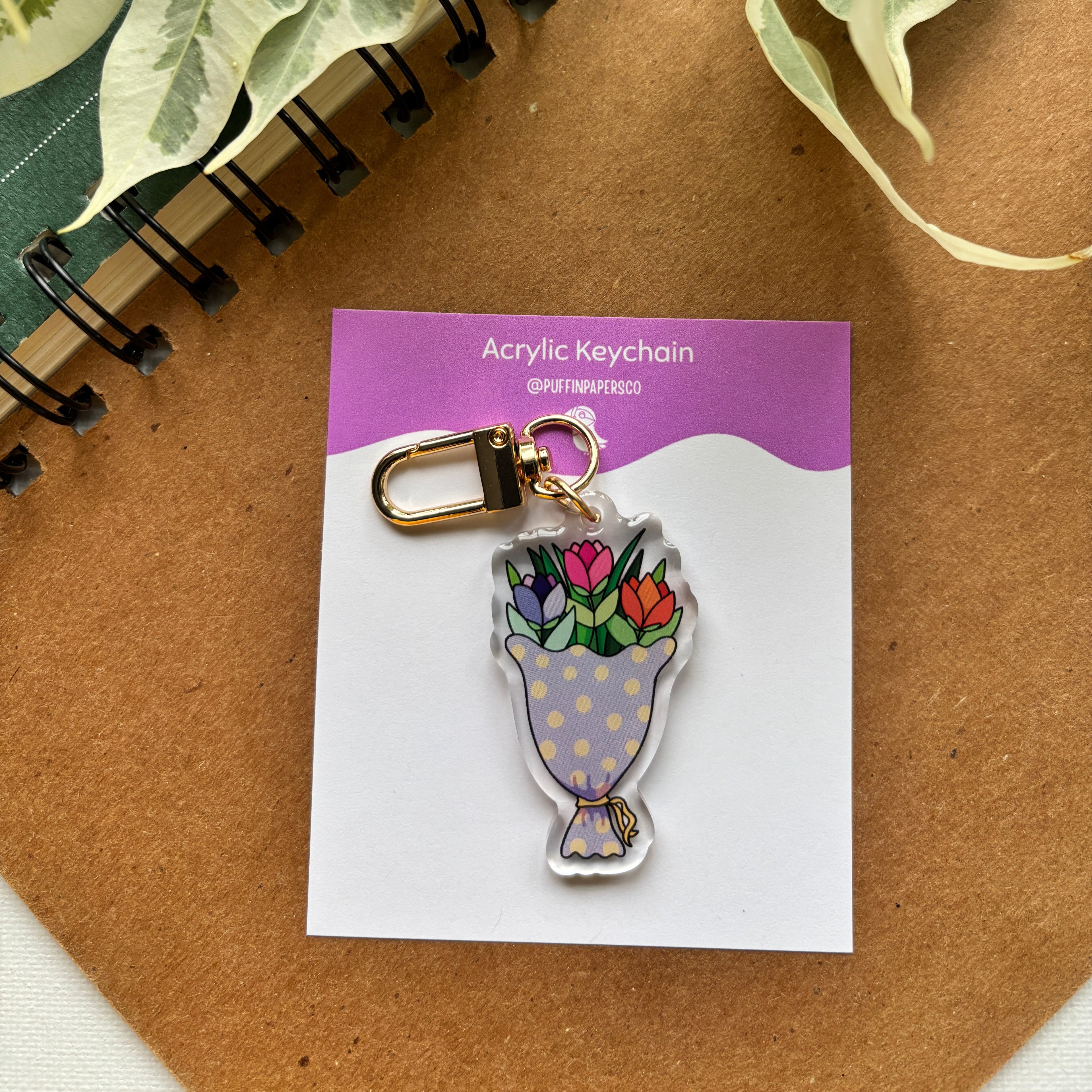 Acrylic keychain with floral design on a card, placed on a brown surface with green leaves.