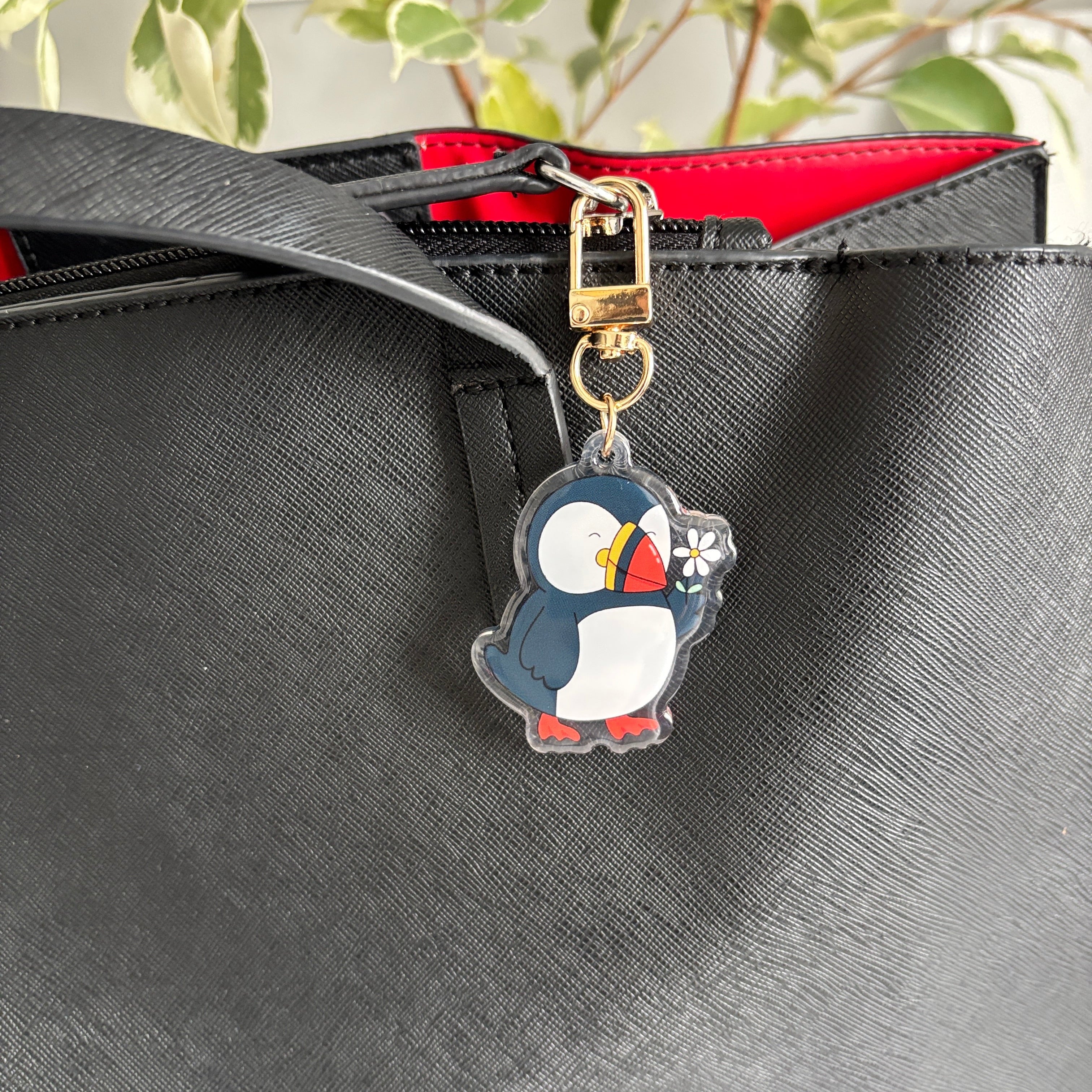 Penguin-shaped keychain attached to a black bag with a red interior.